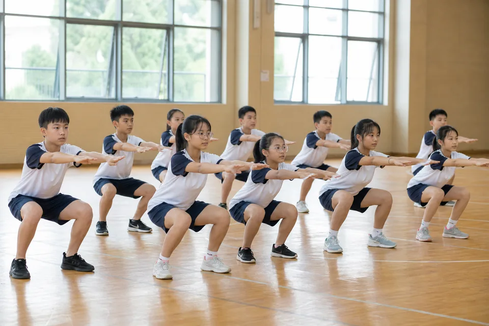 约十名学生在体育馆同步进行徒手深蹲练习